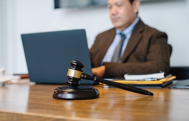 a lawyer sitting at a desk typing on a laptop with a gavel in front of them